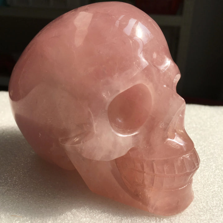 Hand-carved natural rose quartz crystal skull, a polished pink stone sculpture perfect for Reiki healing and home decor.