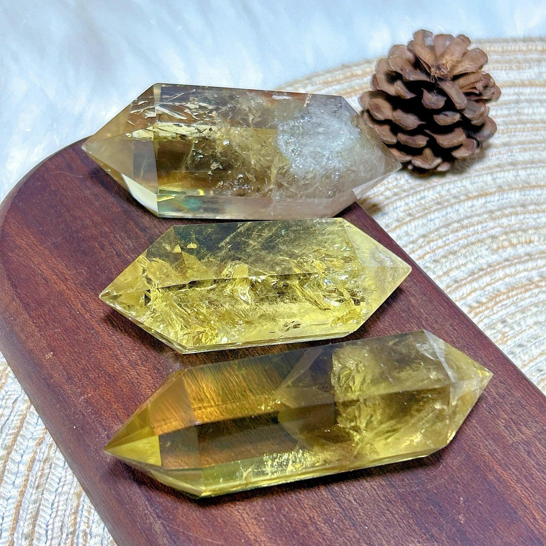 Three natural smokey citrine double tower crystals on a wooden board with a pinecone.