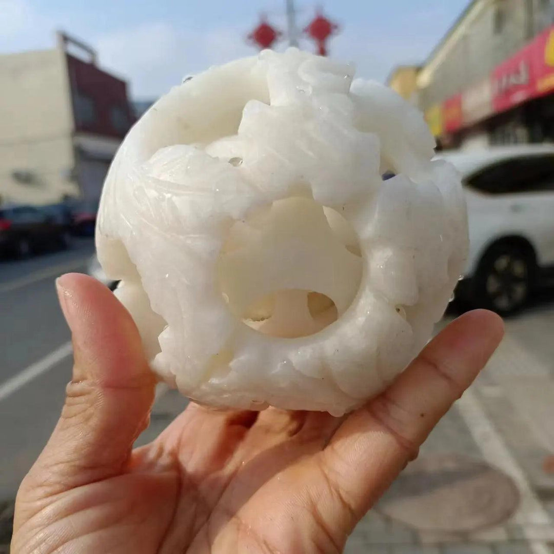 Hand-carved natural white jade crystal ball with intricate openwork design, perfect for reiki healing and energy divination.