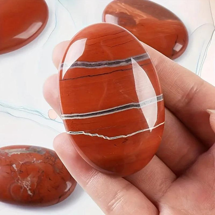 Polished red jasper natural crystal palm stone with healing energy stripes, held in hand.