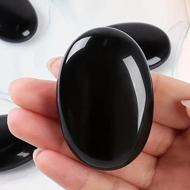 Polished black obsidian palm stone, a smooth oval crystal for stress relief and energy healing.