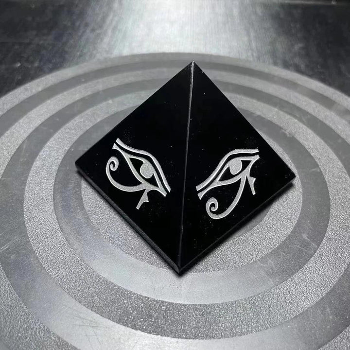 Polished black Obsidian crystal pyramid featuring a protective hand-engraved Eye of Horus symbol for grounding energy.