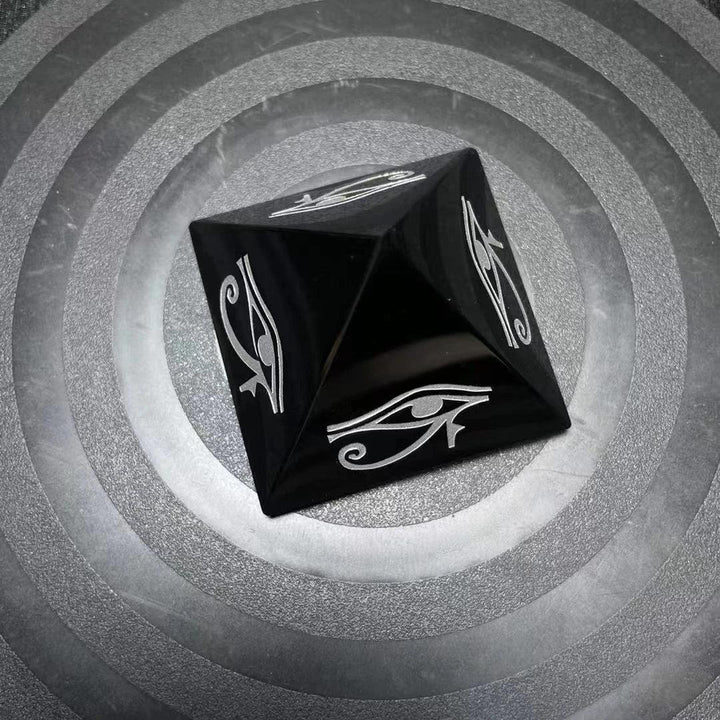 Polished black obsidian pyramid featuring a protective hand-engraved Eye of Horus symbol for grounding and energy shielding.