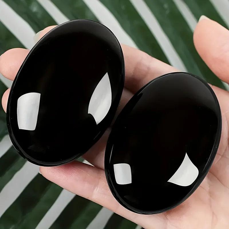 Two polished Obsidian Crystal Palm Stones with a glossy black finish held in a hand for grounding.