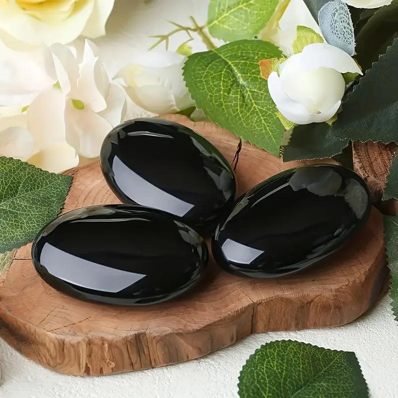 Polished Obsidian Crystal Palm Stones with a glossy black finish on a wooden display.