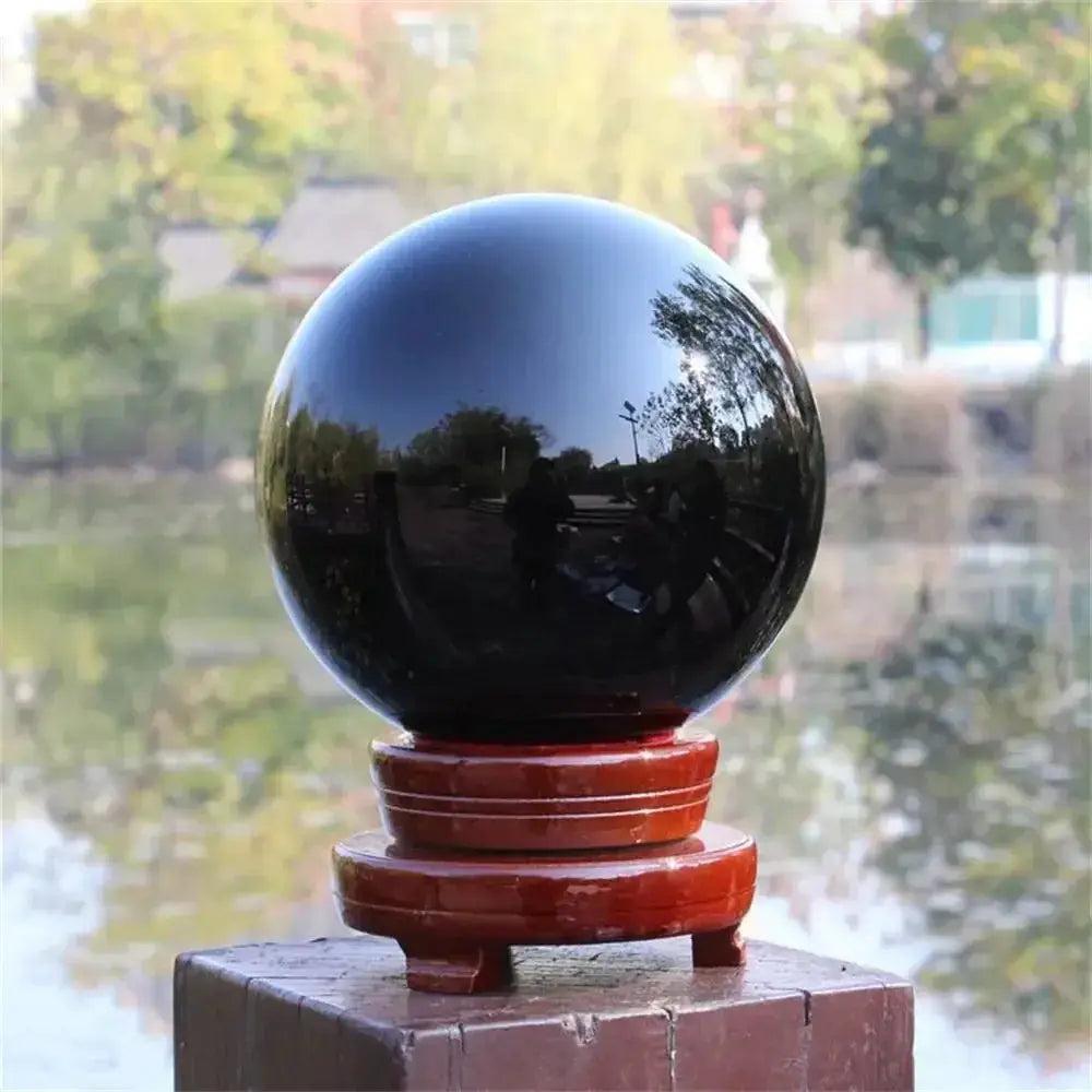 Natural Obsidian Crystal Sphere: Deep jet-black, polished sphere on a wooden stand, reflecting its surroundings.