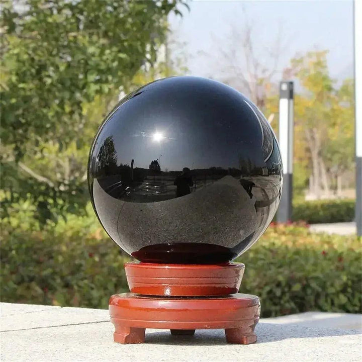 Natural Obsidian Crystal Sphere: Polished jet-black sphere on a wooden stand, reflecting sunlight.