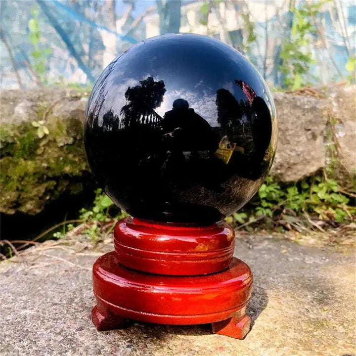 Natural Obsidian Crystal Sphere: Deep jet-black, polished sphere on a red wooden stand, reflecting protective energy.