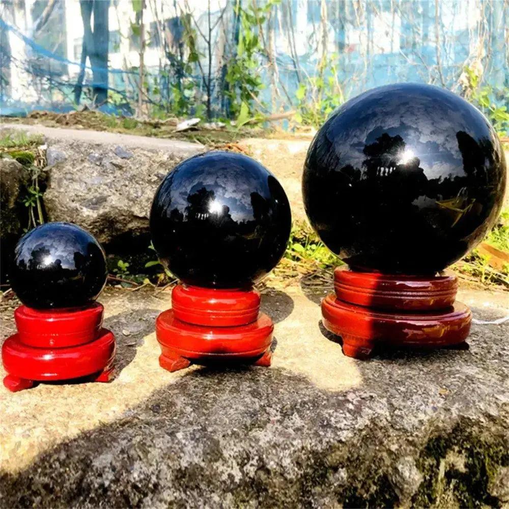 Three polished Natural Obsidian Crystal Spheres of varying sizes on red wooden stands, showcasing deep jet-black color.