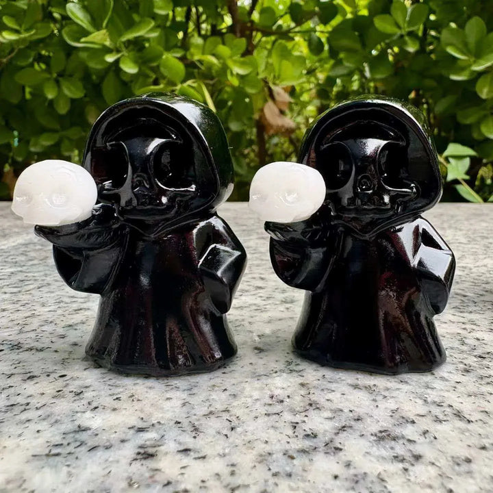 Two black obsidian ghost skull figurines holding small white crystal skulls for healing Halloween home decor.