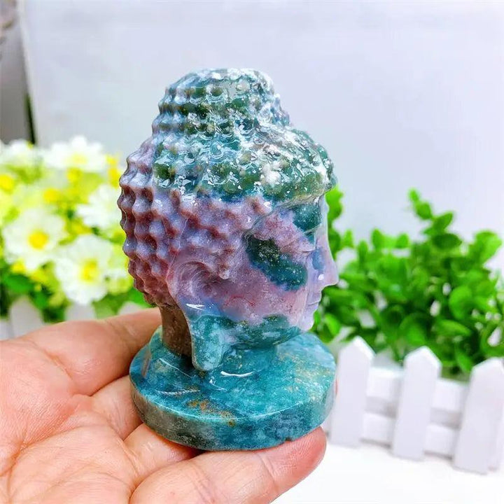 Ocean Jasper Buddha head statue, 80mm, with swirling green, cream, pink, and purple patterns, held in a hand.