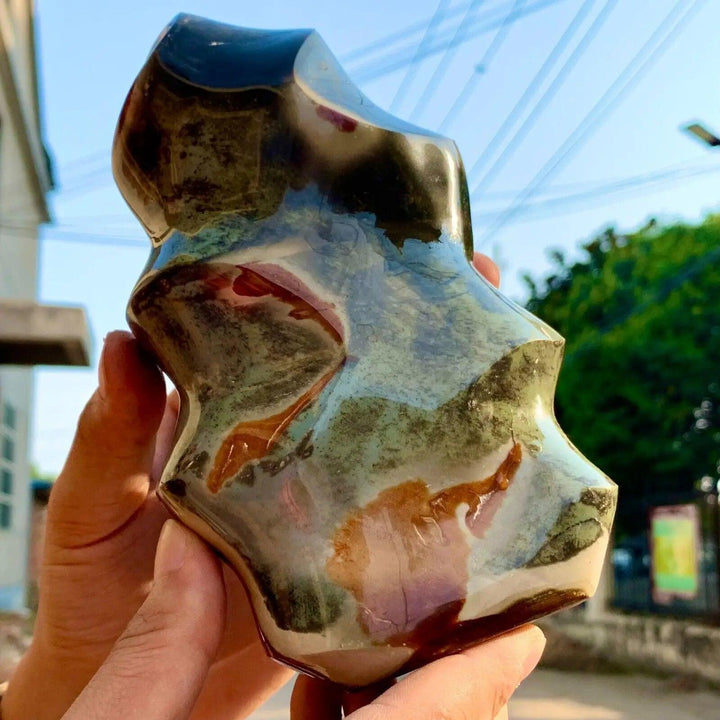 Ocean Jasper flame freeform, showcasing green, brown, and cream orbicular patterns, held outdoors.