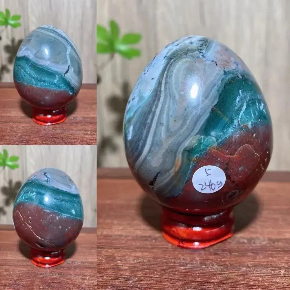 Ocean Jasper crystal egg from Crystal Destiny, featuring greens, reds, and whites on a red stand.