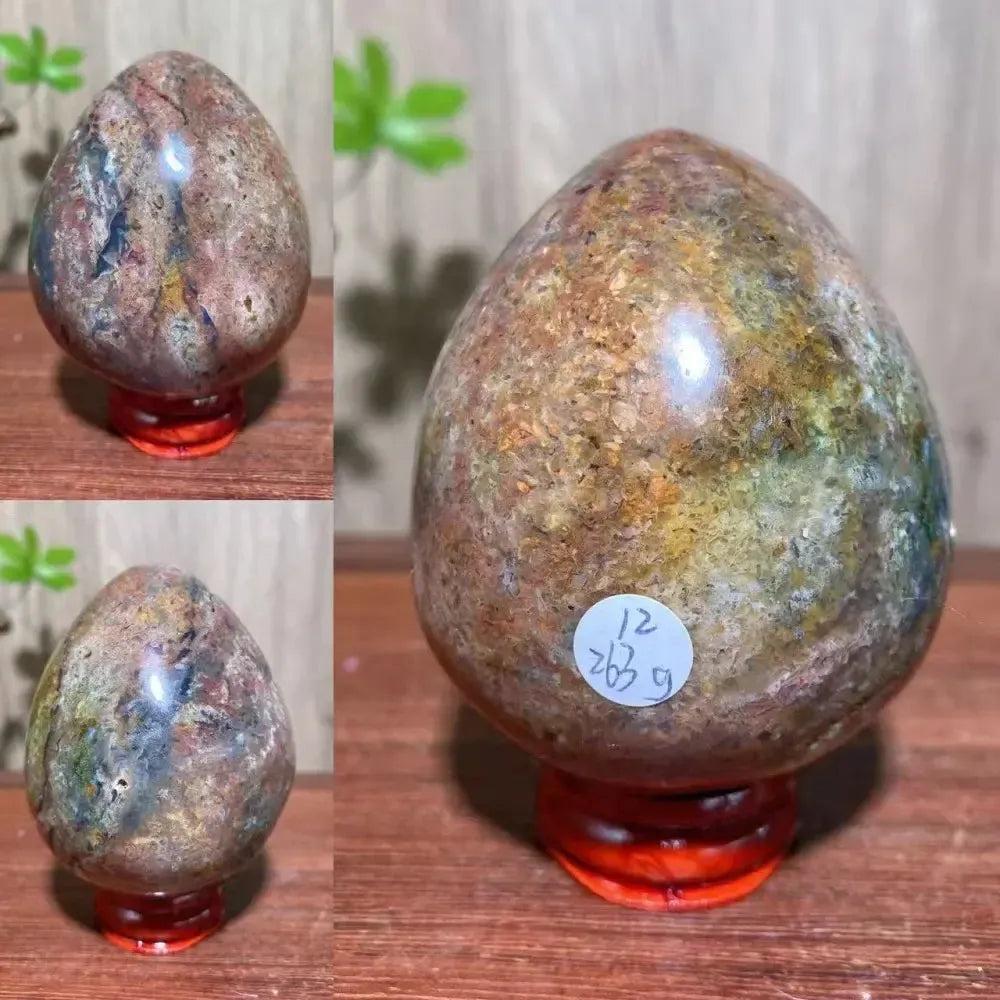 Polished Ocean Jasper crystal egg with earthy browns, greens, and pinks on a red stand from Crystal Destiny.