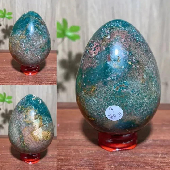 Ocean Jasper crystal egg from Crystal Destiny, featuring swirling greens, pinks, and browns on a red stand.