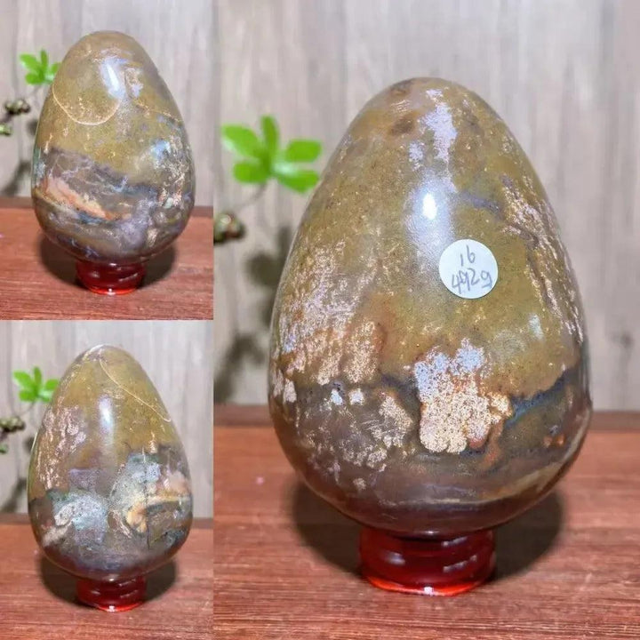 Polished Ocean Jasper crystal egg from Crystal Destiny, displaying earthy greens, browns, and peachy pinks on a red stand.