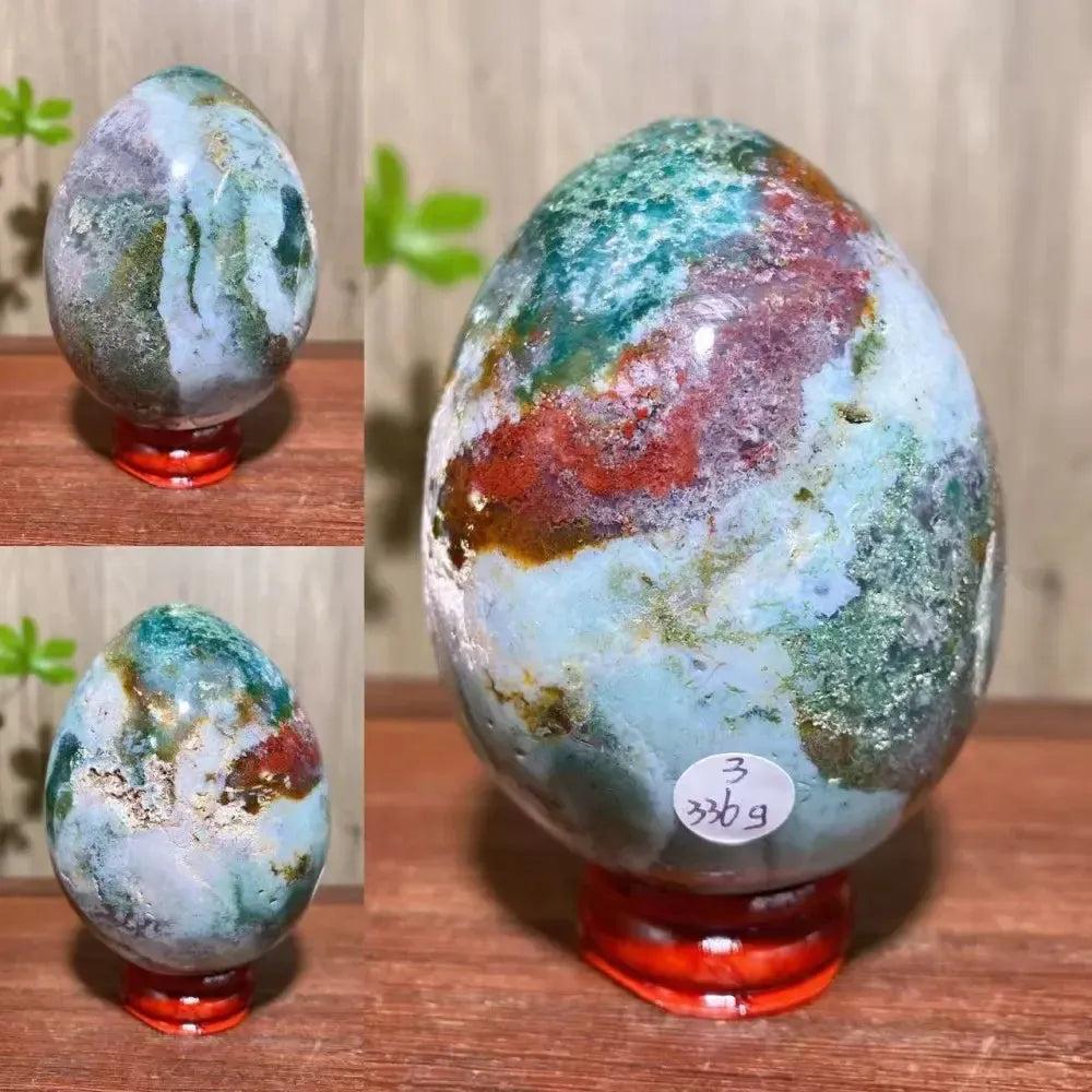 Ocean Jasper crystal egg from Crystal Destiny, featuring swirling greens, reds, and blues on a red stand.