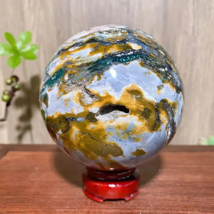 Ocean Jasper Sphere XXL: stunning orbicular greens, pinks, creams, yellows, earth tones with a natural cavity on a red stand.