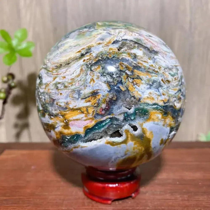 Ocean Jasper Sphere XXL: Orbicular greens, pinks, creams, yellows, and earth tones on a red stand.