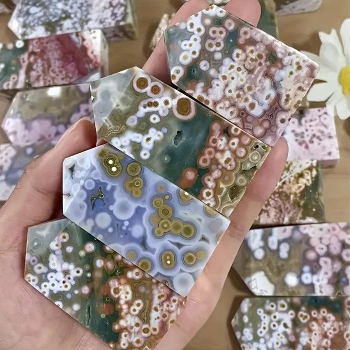 Hand holding five colorful Ocean Jasper crystal towers with unique orbicular patterns.
