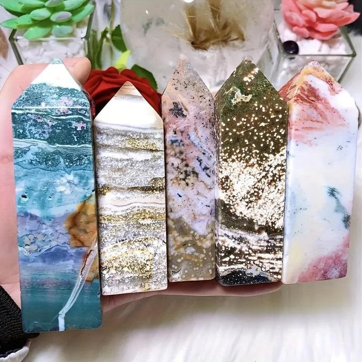 Five polished Ocean Jasper crystal towers in varied colors and patterns, held in a hand.