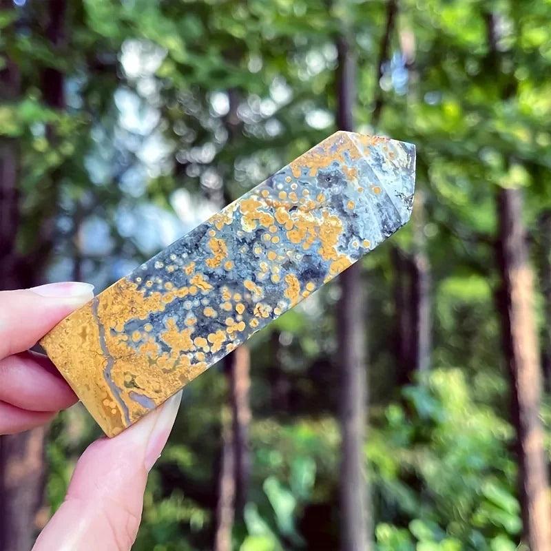Ocean Jasper crystal tower with yellow, gray, and black orbicular patterns, held outdoors.