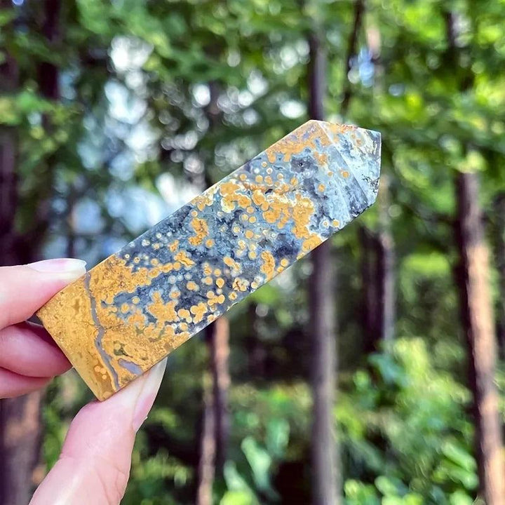 Ocean Jasper crystal tower with yellow, gray, and black orbicular patterns, held outdoors.