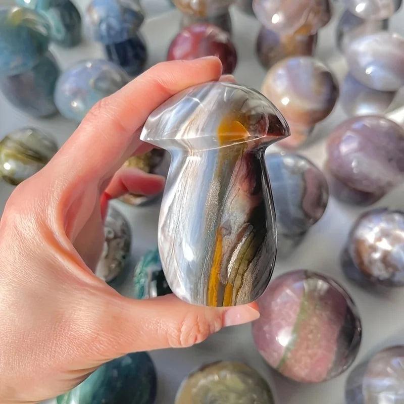Hand holding an Ocean Jasper mushroom crystal carving with sage, cream, and rust swirls, promoting joy and calm.