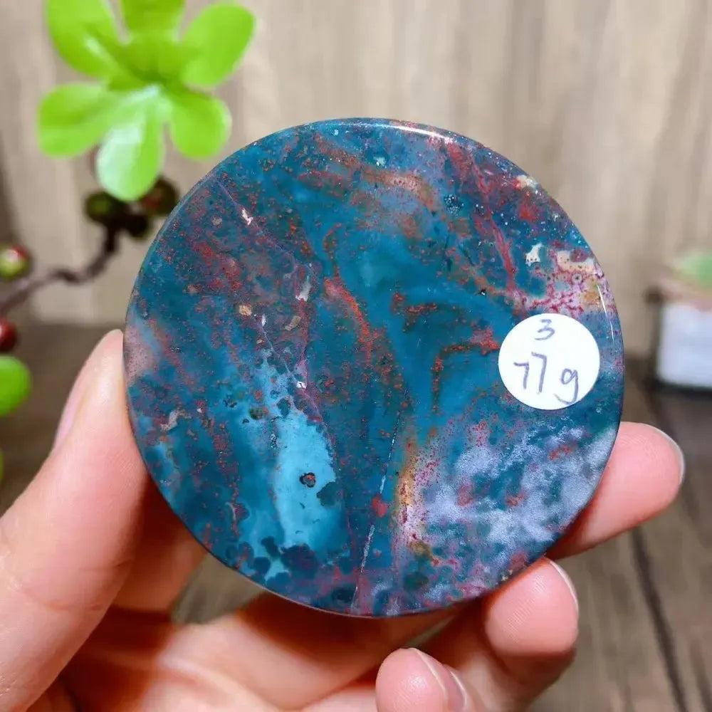 Crystal Destiny Bloodstone round slice, vibrant teal with red flecks, held in hand.