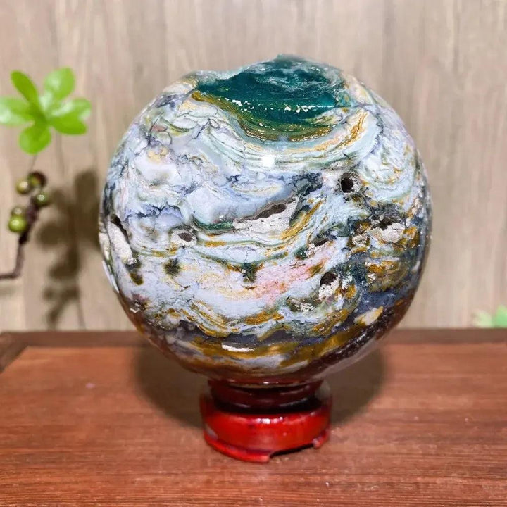 Crystal Destiny's XXL Ocean Jasper sphere with vibrant green, pink, cream, and yellow patterns on a red stand.
