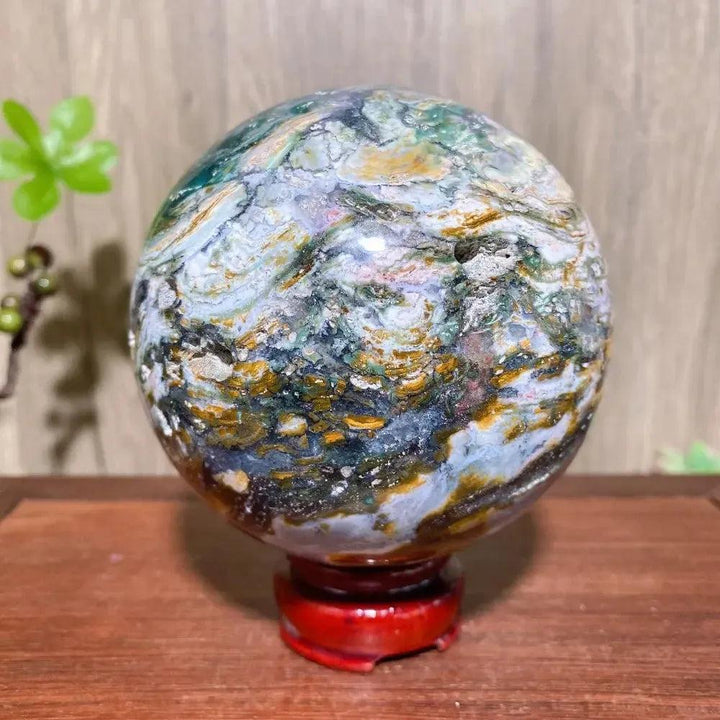 Ocean Jasper Sphere XXL from Crystal Destiny, showcasing vibrant greens, pinks, and yellows on a red stand.