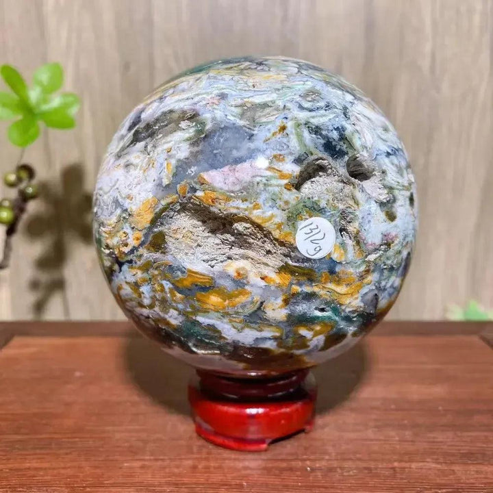 Crystal Destiny's XXL Ocean Jasper sphere with vibrant greens, pinks, and yellows on a red stand.