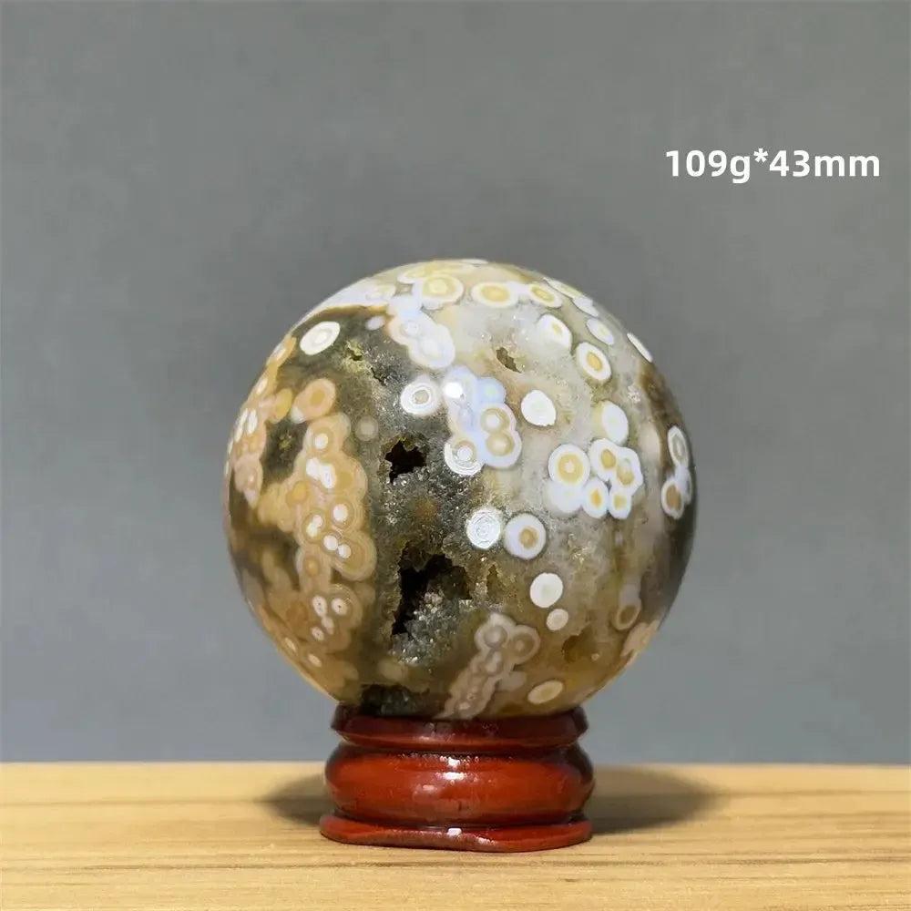 Ocean Jasper sphere with orbicular patterns in green, white, cream, pink, and red, on a red display base.