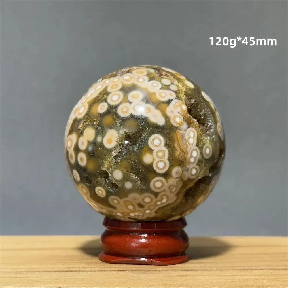 Ocean Jasper sphere with green, white, and cream orbicular patterns on a red wooden base from Crystal Destiny.