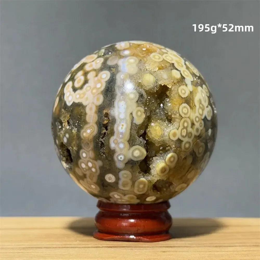 Ocean Jasper sphere with orbicular patterns in green, white, cream, pink, and red, on a red wooden base. Crystal Destiny.