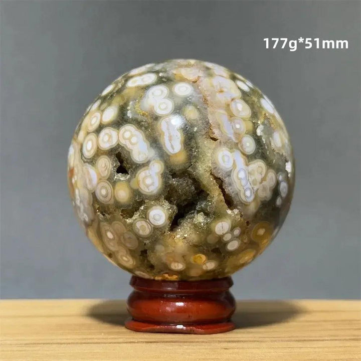 Ocean Jasper sphere from Crystal Destiny with green, white, cream, pink, and red orbicular patterns on a wood base.
