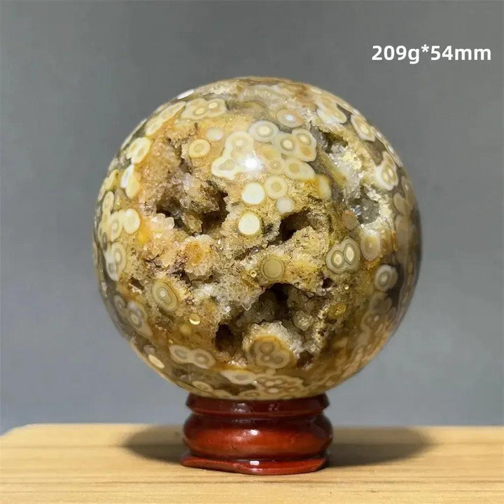 Ocean Jasper sphere with orbicular patterns in green, white, cream, pink, and red, on a red wooden base.