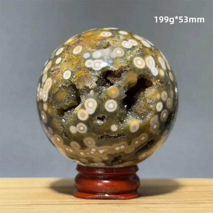 Ocean Jasper sphere with green, white, and cream orbicular patterns, displayed on a red wooden base.