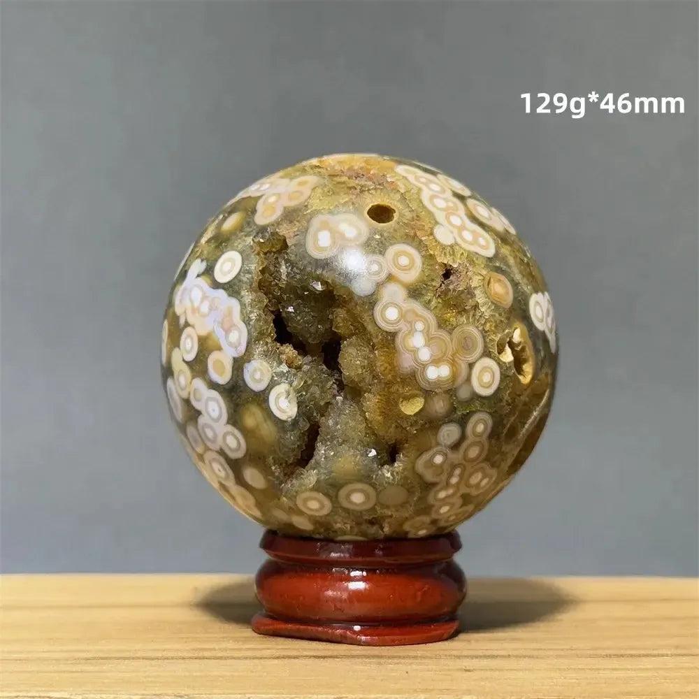 Ocean Jasper sphere from Crystal Destiny, with green, white, cream, pink, and red orbicular patterns, on a red base.