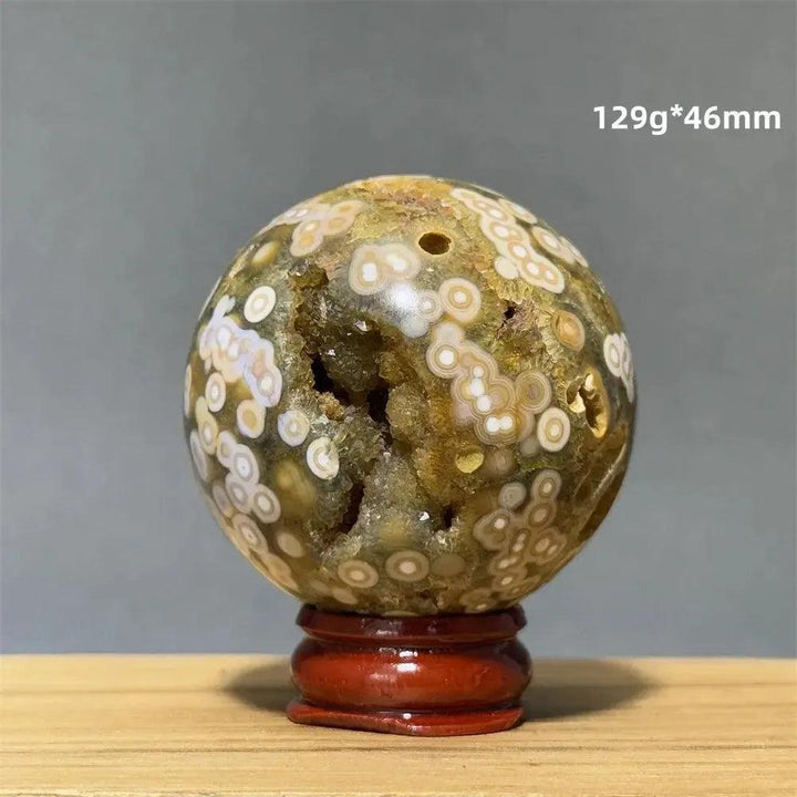 Ocean Jasper sphere from Crystal Destiny, with green, white, cream, pink, and red orbicular patterns, on a red base.