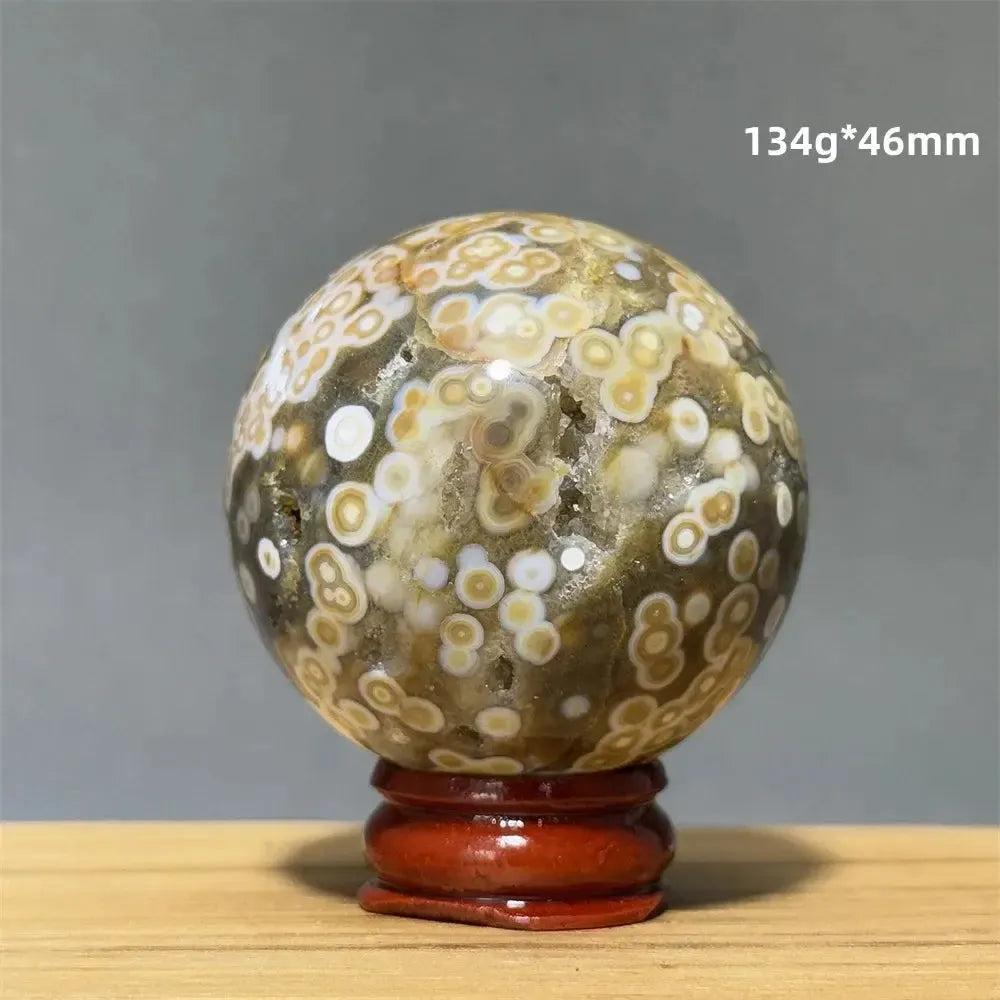 Ocean Jasper sphere with orbicular patterns in green, white, cream, pink, and red on a red wooden base.