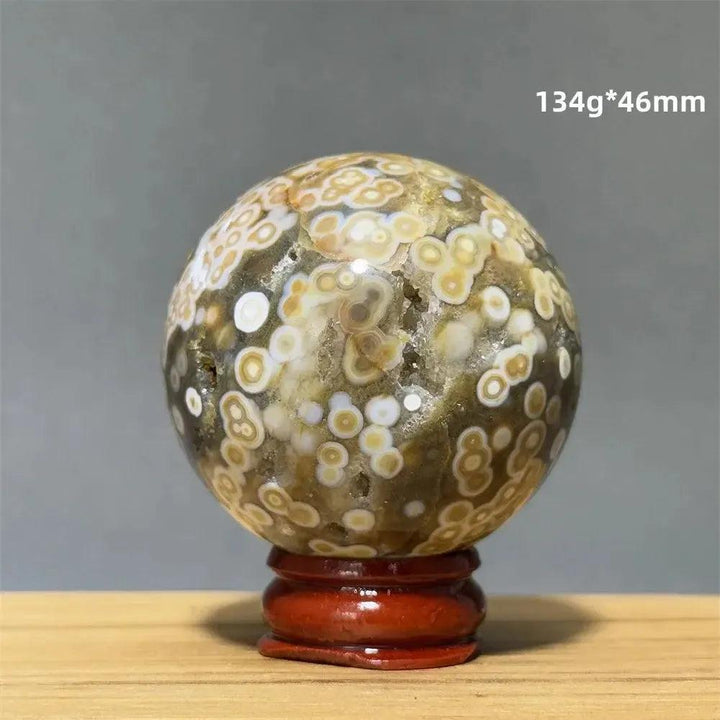Ocean Jasper sphere with orbicular patterns in green, white, cream, pink, and red on a red wooden base.