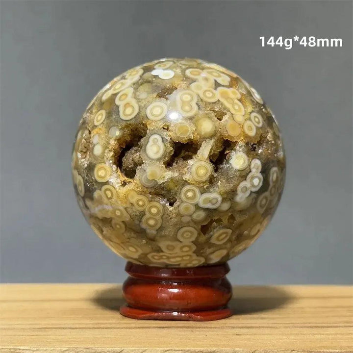 Ocean Jasper sphere with orbicular patterns in green, white, cream, pink, and red on a wooden base.