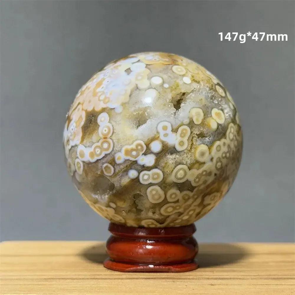 Ocean Jasper sphere with orbicular patterns in green, white, cream, pink, and red on a red display base.