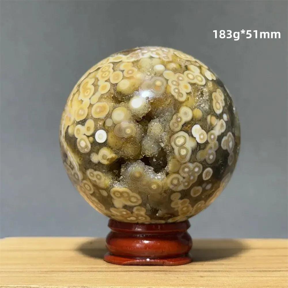 Ocean Jasper sphere with orbicular patterns in green, white, cream, pink, and red on a red wooden base.