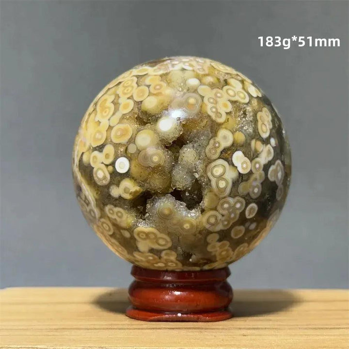 Ocean Jasper sphere with orbicular patterns in green, white, cream, pink, and red on a red wooden base.
