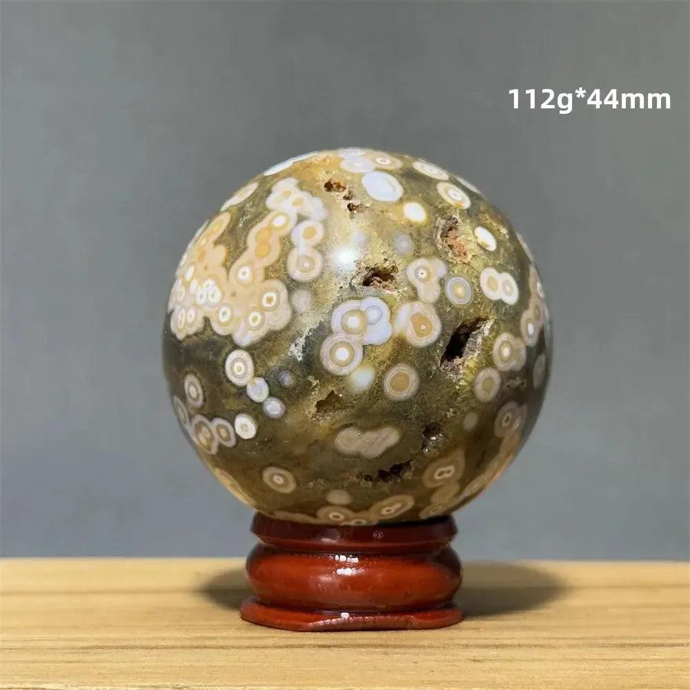 Ocean Jasper sphere with green, white, cream, pink, and red orbicular patterns on a wooden base from Crystal Destiny.