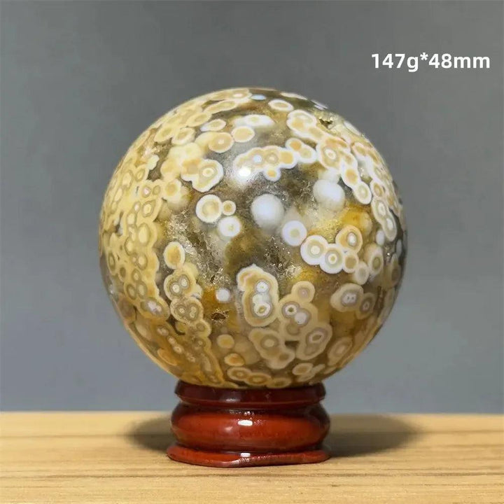 Ocean Jasper sphere from Crystal Destiny, with green, white, cream, pink, and red orbicular patterns on a wood base.