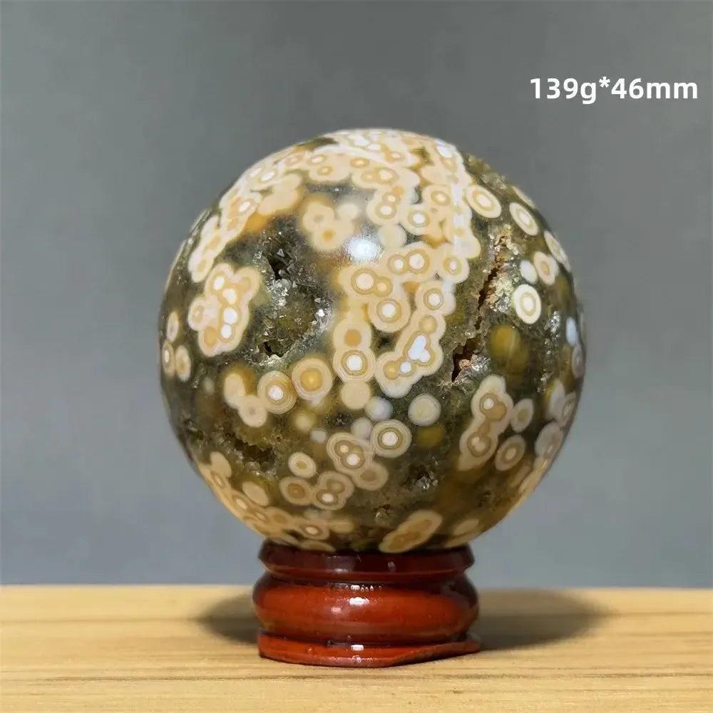 Ocean Jasper sphere, green, white, cream, pink orbicular patterns, on a red wooden base from Crystal Destiny.