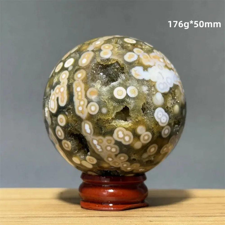 Ocean Jasper sphere from Crystal Destiny, featuring green, white, and cream orbicular patterns on a red base.